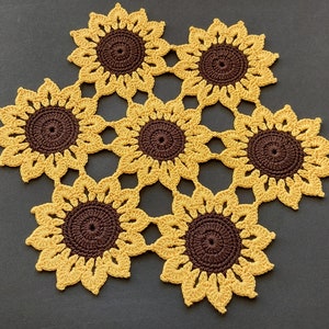 Può includere: Un runner da tavolo all'uncinetto con sei girasoli marroni e gialli.