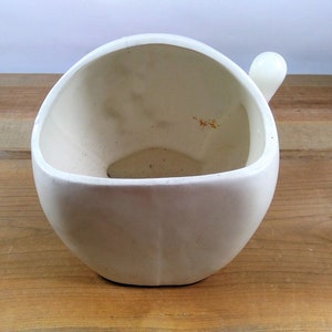 May include: White ceramic planter with a rounded shape and a small handle on the side.
