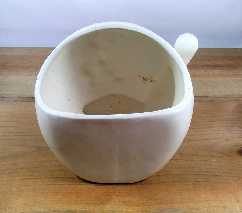 May include: White ceramic planter with a rounded shape and a small handle on the side.