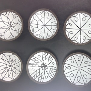 May include: Six white ceramic plates with black geometric designs. The plates are arranged in two rows of three, with the designs varying on each plate.