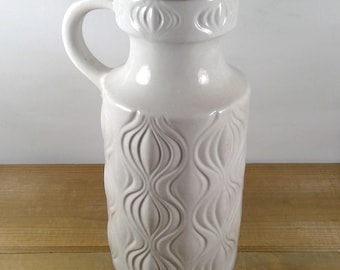 May include: White ceramic vase with a textured, wavy design. The vase has a handle and a wide opening.