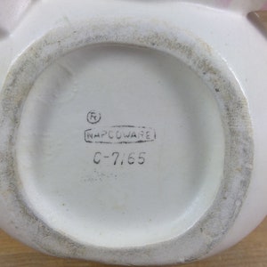 May include: White ceramic pitcher with a pink handle and a black stamp on the bottom that reads "(R) NAPCCOWARE C-7165".