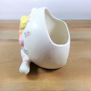 May include: White ceramic planter shaped like a girl's head with pink, yellow, and blue painted details. The planter has a wide opening for planting.