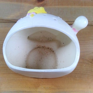 May include: White ceramic planter shaped like a bird with a yellow beak and pink accents. The planter has a hole in the bottom for drainage.