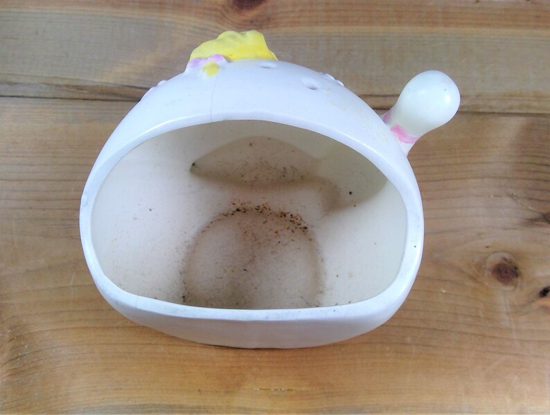 May include: White ceramic planter shaped like a bird with a yellow beak and pink accents. The planter has a hole in the bottom for drainage.