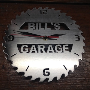 May include: A silver metal clock shaped like a saw blade with black hands and the text "Bill's Garage" in the center.