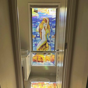 Può includere: Una finestra in vetro colorato che raffigura una sirena su uno sfondo colorato. La luce del sole splende attraverso la finestra, proiettando un motivo arcobaleno sul pavimento.