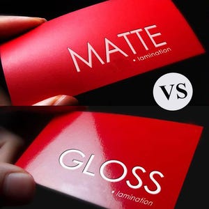 May include: A comparison of red business cards with white text. One card reads "MATTE" with "lamination" below. The other card reads "GLOSS" with "lamination" below. A white circle with "VS" is between the cards.