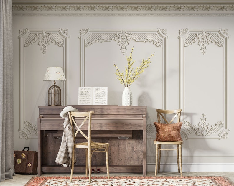 May include: A vintage-style piano with a wooden top and a white lamp with a birdcage shade. Two chairs with brown cushions are placed in front of the piano. The room has white walls with ornate molding and a rug with a floral pattern.