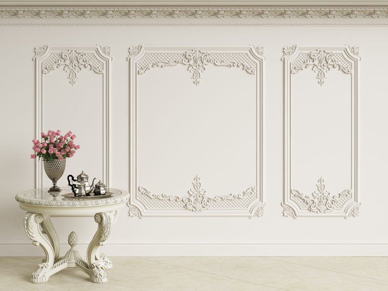May include: A white table with ornate legs and a marble top. A bouquet of pink roses in a silver vase and a silver tea set are on the table. The table is in front of a white wall with ornate molding.