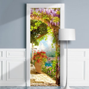 Pode incluir: Um adesivo de porta que apresenta um arco floral colorido com vista para uma cidade costeira. O arco &eacute; coberto de flores de glicinia roxas e videiras verdes. Um vaso vermelho com uma planta fica na frente do arco.