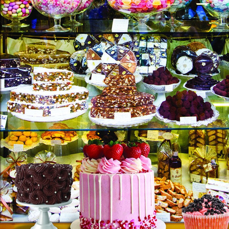 Puede incluir: Una vitrina de vidrio llena de varios pasteles y postres. La estanter&iacute;a superior presenta una variedad de caramelos coloridos, mientras que la estanter&iacute;a inferior muestra un pastel rosa con fresas, un pastel de chocolate con remolinos y una peque&ntilde;a magdalena con chispas de chocolate.