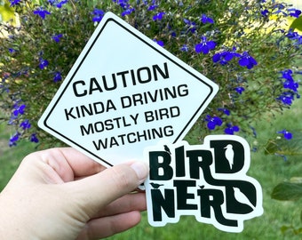May include: A white diamond-shaped sticker with black text that reads "Caution Kinda Driving Mostly Bird Watching". A black and green sticker with the text "Bird Nerd" and a silhouette of a bird in the "D" is partially visible.