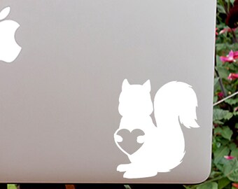 May include: A white laptop computer with a white apple logo and a white silhouette of a squirrel holding a heart on the lid.