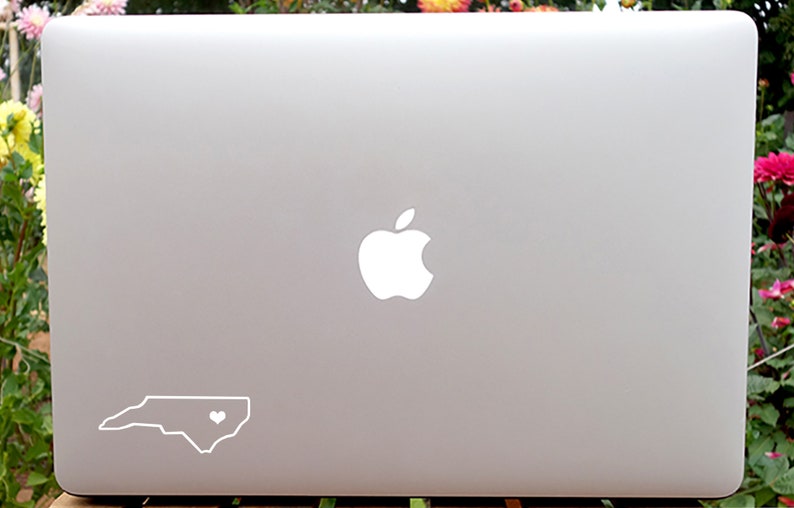 May include: A silver laptop computer with a white Apple logo and a white outline of the state of North Carolina with a heart in the center.
