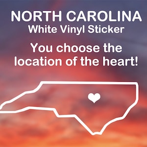 May include: White vinyl sticker of the state of North Carolina with a heart in the center. The text "NORTH CAROLINA" and "White Vinyl Sticker" is at the top of the image. The text "You choose the location of the heart!" is below the state outline.