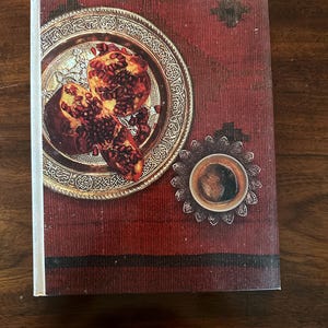 Op de afbeelding: Een close-up van een gouden bord met twee halve granaatappels op een rode achtergrond. Een klein kopje koffie staat op een decoratief zilveren dienblad.