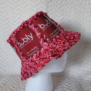 May include: A pink crocheted bucket hat made from recycled Bubly sparkling water cans. The cans have the text "bubly" and "cherrybubly" printed on them.