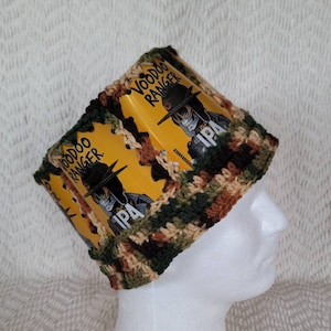 May include: A crocheted hat with a camouflage pattern. The hat is made with beer can tabs featuring the Voodoo Ranger IPA logo.