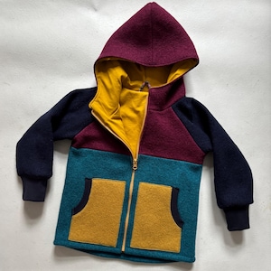 Könnte beinhalten: Eine mehrfarbige Kapuzenjacke mit Reißverschluss. Die Jacke ist aus einem weichen, strukturierten Stoff gefertigt und hat eine Farbkombination aus Dunkelblau, Burgunderrot, Türkis und Senfgelb. Die Jacke hat eine große Tasche auf der Vorderseite und eine Kapuze mit Futter.