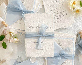 Puede incluir: Conjunto de invitaciones de boda con cinta azul y papel blanco. La invitación incluye el texto "Se solicita la presencia de usted en la boda de Katherine Nisme Affman y Alex Chaom. Jueves 19 de mayo de 2019 a las 5:00 p.m. República Dominicana. Hora de cóctel y recepción posterior. Traje de etiqueta."