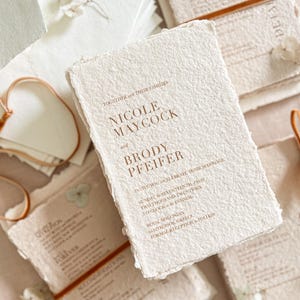 Luxury handmade paper wedding invitation suite styled with warm terracotta silk ribbon, textured cotton deckle edge paper cards and elegant minimalist typography design.
