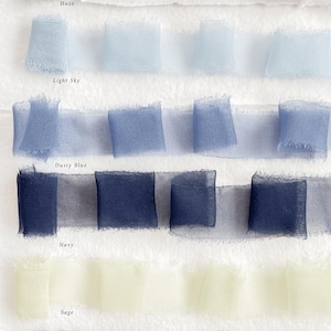 May include: Fabric ribbons in shades of Haze, Light Sky, Dusty Blue, Navy, Sage, and Forest. The ribbons are arranged in folded squares, with the colour names printed below each row. Ideal for craft projects.