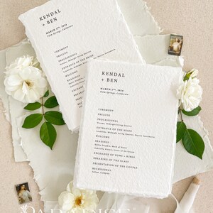 May include: A wedding ceremony program with a white background and black text. The program lists the order of events for the wedding ceremony, including the processional, entrance of the bride, readings, exchange of vows, and recessional. The program is decorated with a simple, elegant design.