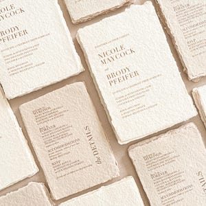 Fine art wedding invitation suite including handmade deckle edge invitation, RSVP cards, details cards and silk ribbon styling arranged in editorial flat lay.