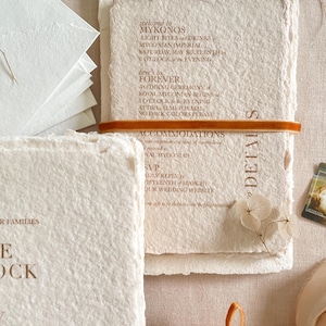 Close-up of colored handmade cotton paper wedding invitation showing natural deckle edges, soft paper fibers and warm terracotta letterpress-style typography.