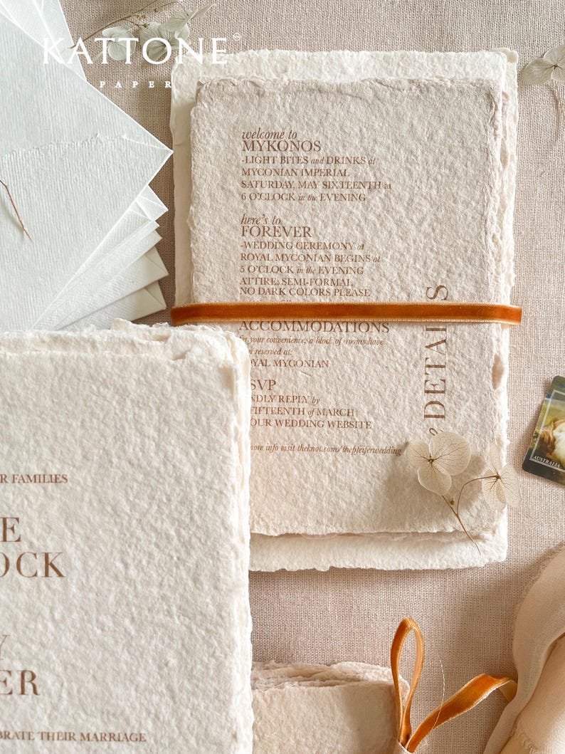 Close-up of colored handmade cotton paper wedding invitation showing natural deckle edges, soft paper fibers and warm terracotta letterpress-style typography.