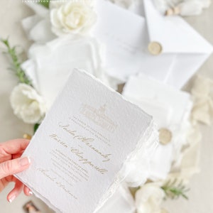 May include: White wedding invitation with gold lettering. The invitation reads "The honor of your presence is requested at the marriage of Sasha (Hernandez) and Warren Chiapparelli. Saturday, the first of April, five o'clock in the afternoon, Sand and Twenty Three, Krogia Bantiarg Apostol, Tequila, Jalisco Mexico. Reception to follow.  Cacanda et Drapenario."