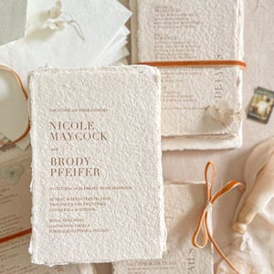 Close-up of colored handmade cotton paper wedding invitation showing natural deckle edges, soft paper fibers and warm terracotta letterpress-style typography.