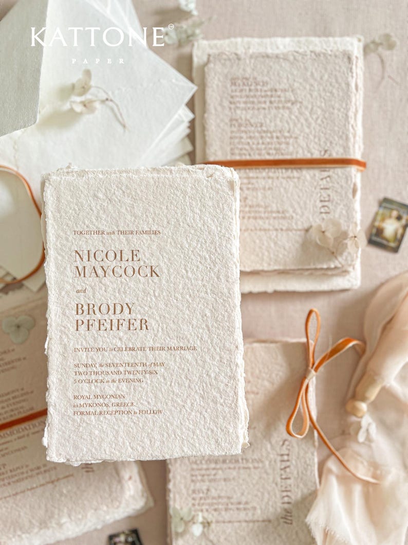 Close-up of colored handmade cotton paper wedding invitation showing natural deckle edges, soft paper fibers and warm terracotta letterpress-style typography.