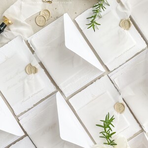 May include: White wedding invitations with white envelopes and wax seals. The invitations are decorated with sprigs of rosemary and white roses.