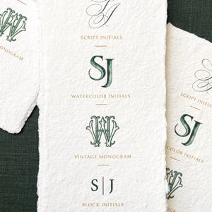 May include: Off-white paper cards with green and gold monogram designs. The cards display script, watercolour, and block initials, with text labels including "Script Initials" and "Watercolor Initials". The cards are on a dark green surface.