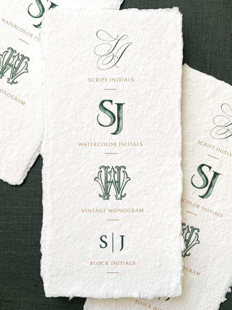 May include: Off-white paper cards with green and gold monogram designs. The cards display script, watercolour, and block initials, with text labels including "Script Initials" and "Watercolor Initials". The cards are on a dark green surface.