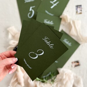 May include: Green table number cards with white calligraphy. The cards are numbered 3, 4, and 5. The text "Table" is written on each card.
