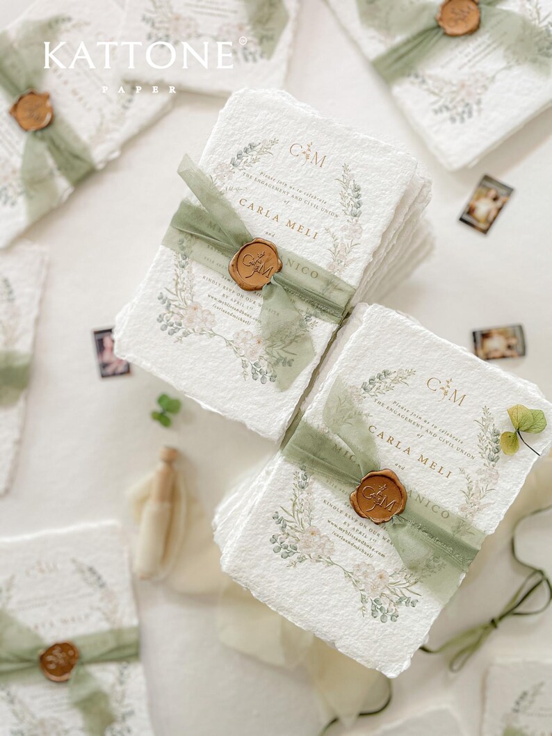 May include: A stack of white, textured paper invitations with a green ribbon and a wax seal. The invitations feature a floral design and the text "Carla Meli & Nico".