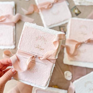 This exquisite handmade paper wedding invitations suite offers a blend of classic elegance and personalized artistry. Each bespoke invites set features a custom, hand-painted watercolor monogram of your initials, creating a unique and personal touch. The invitations are beautifully assembled with luxurious satin silk ribbons, adding a soft, opulent texture that your guests will adore.