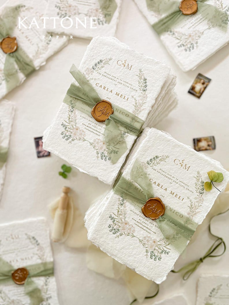 May include: A stack of white paper invitations with green and gold accents. The invitations feature a floral design with the text "Please join us as we celebrate the engagement and civil union of Carla Meli and Nico" and the date "Saturday, 29th April 2023".