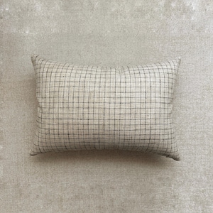 May include: Rectangular pillow with a beige background and a black grid pattern. The pillow has a soft, textured appearance and is likely made of fabric. The grid pattern is evenly spaced, creating a simple, yet stylish design. This pillow is suitable for home decor.
