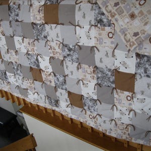 May include: A handmade patchwork quilt with a matching pillow. The quilt features squares of white, gray, and brown fabric, some with animal prints. The squares are tied together with brown yarn. The quilt is approximately 60 inches by 70 inches.
