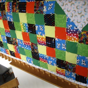May include: A colorful patchwork quilt with squares of various patterns and colors, including red, green, blue, and yellow. Some squares feature cow prints and other designs. The quilt is trimmed with a white border.