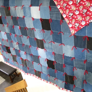 May include: A patchwork quilt constructed from various shades of blue and black denim squares, joined together with visible red yarn ties. The reverse side of the quilt features a red fabric with a repeating pattern of cartoon dogs and white stars.