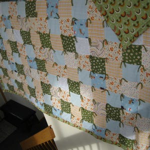 May include: A patchwork quilt with a variety of patterned squares in shades of green, blue, and beige. The quilt features a repeating pattern of squares, with a green border and a separate green patterned section.