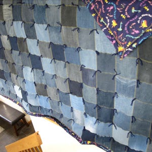 May include: A patchwork quilt constructed from square denim fabric pieces in various shades of blue, joined with dark blue yarn ties. The quilt features a dark blue backing fabric printed with colorful illustrations and the text Oh, the Places You'll Go.