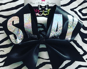 Puede incluir: Lazo de animadora negro con un diseño de "SLAY" en purpurina plateada. El lazo está hecho de un material brillante, similar al satén.
