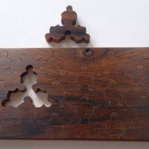 May include: A wooden jigsaw puzzle with a missing piece and a separate piece above. The puzzle is made of dark brown wood with visible grain. The puzzle pieces are shaped like people. The missing piece is in the center of the puzzle.