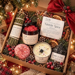 May include: A holiday gift box containing a cedar smudge stick, a 4 oz jar of peppermint scrub, a bag of Yuletide Spice potpourri, a pink bath bomb, a 4 oz vanilla candle, and a black Lump a Coal sea salt soap bar.